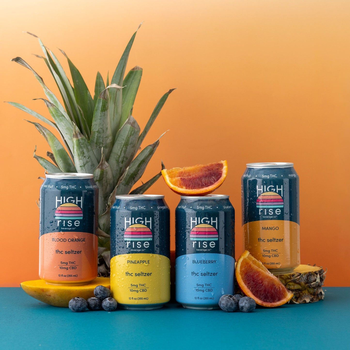 Cans of High Rise Sunset Sampler (Blood Orange, Pineapple, Blueberry and Pineapple) surrounded by fresh fruit on an orange and blue background.
