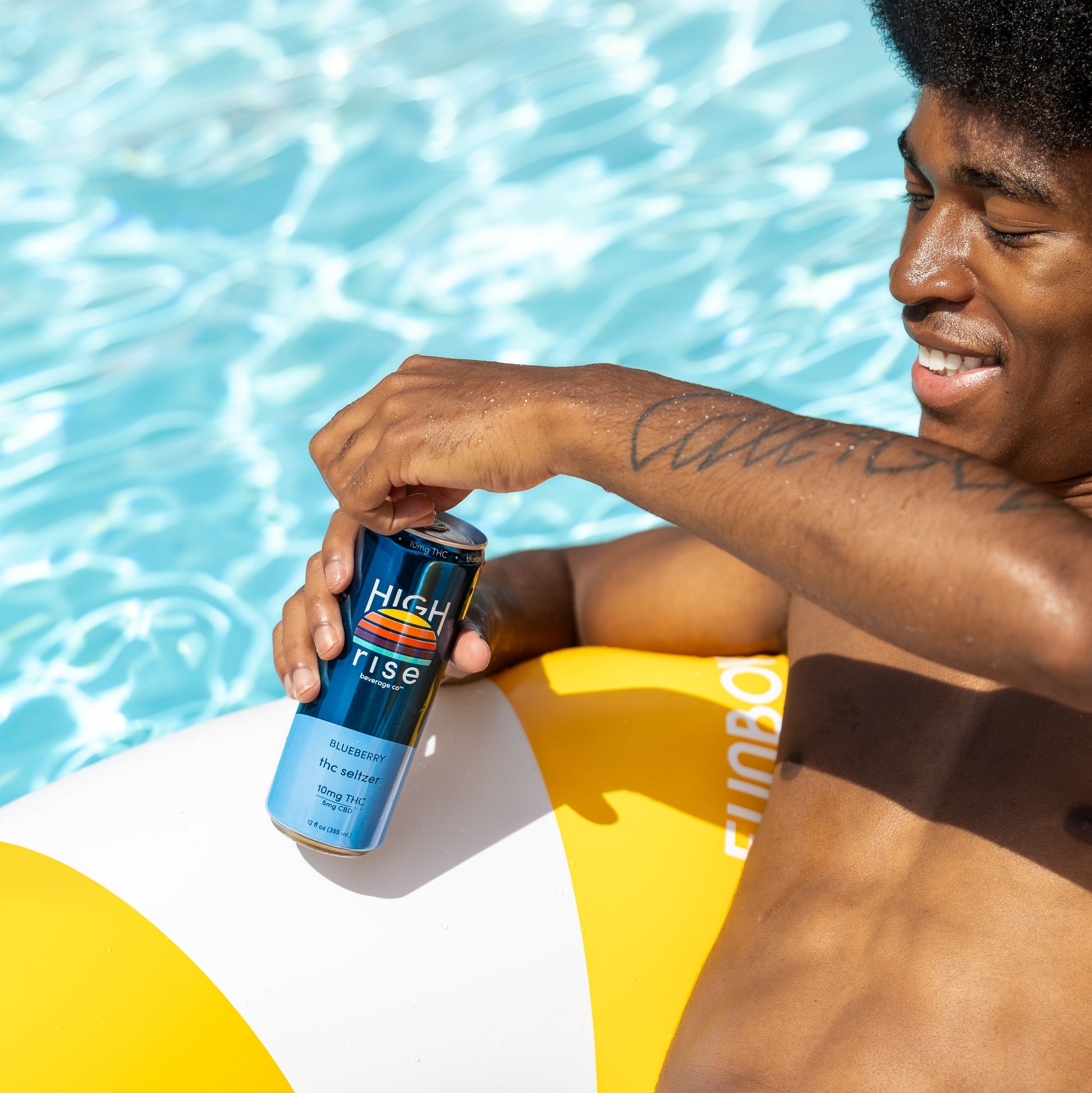 Man by a pool holding a can of High Rise Blueberry THC Seltzer.  