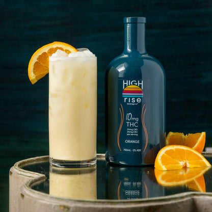 High Rise 10mg Orange Inusion bottle next to a mocktail with an orange slice on a reflective surface.