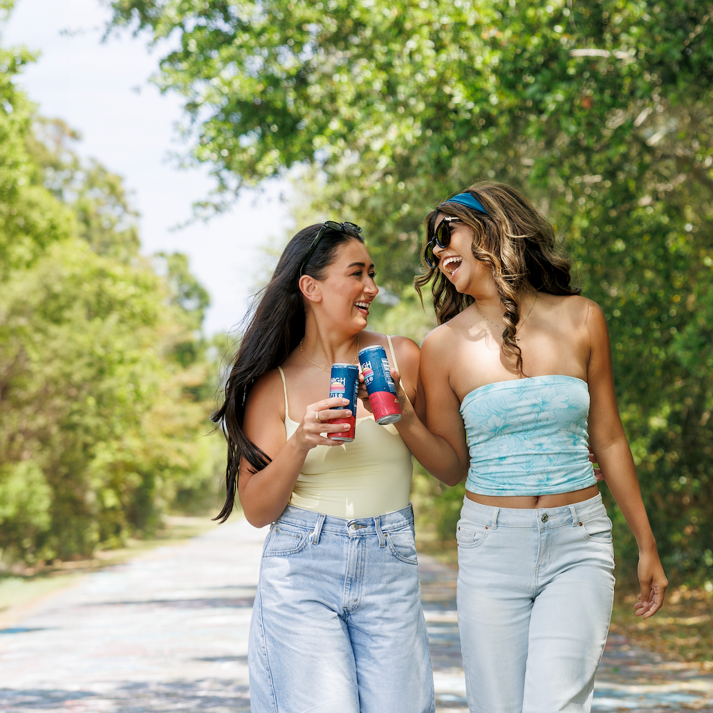 Two women walking down graffiti road drinking High Rise Raspberry THC Seltzers 