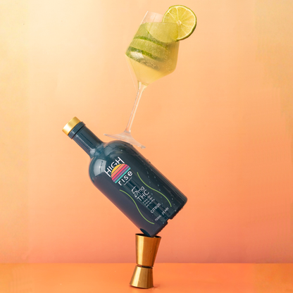 Bottle of High Rise THC Infuion with a mocktail glass filled with limes and lime wedge on an orange gradient background.