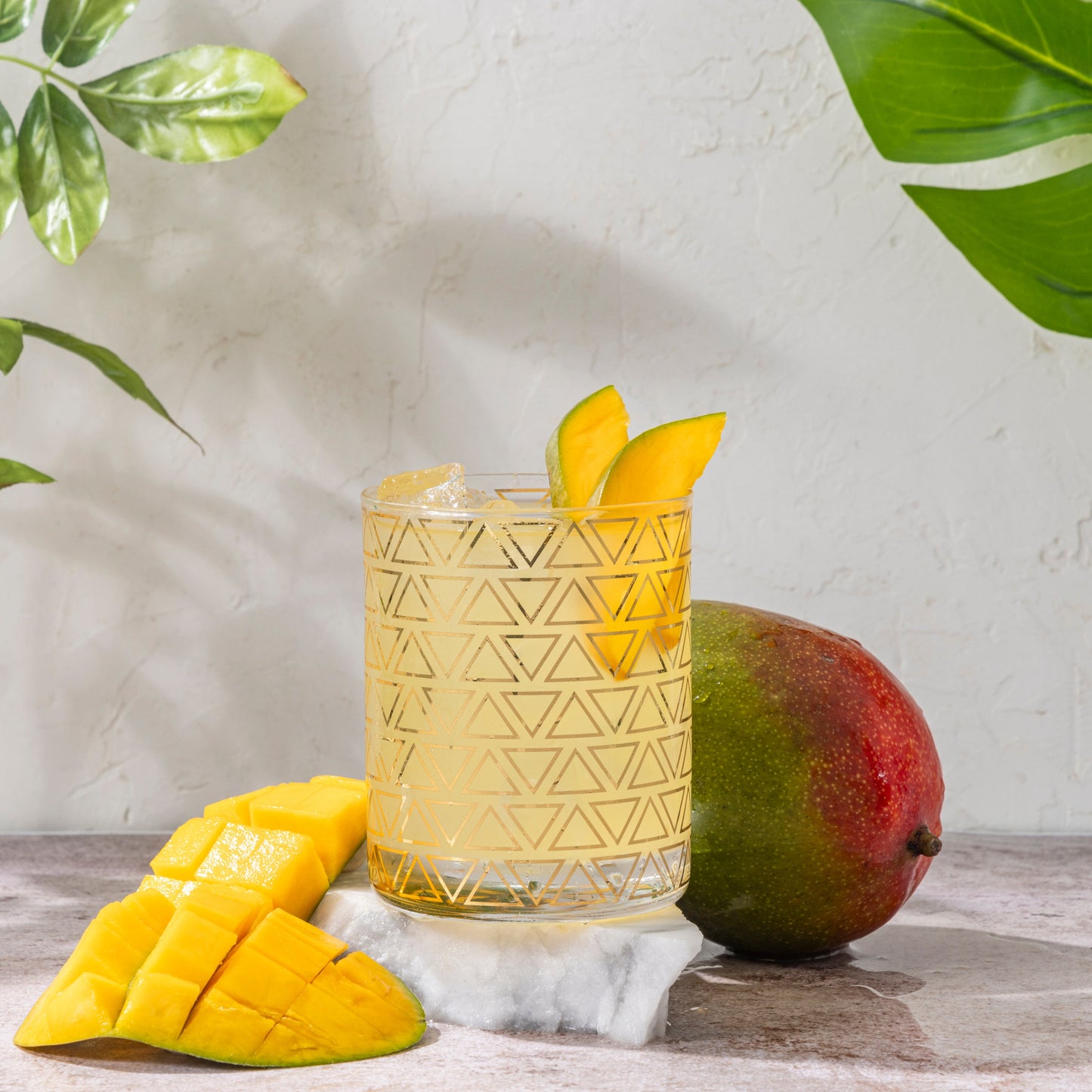 High Rise 3mg THC Mango seltzer in a glass with mango slices and a whole mango on a wooden surface.