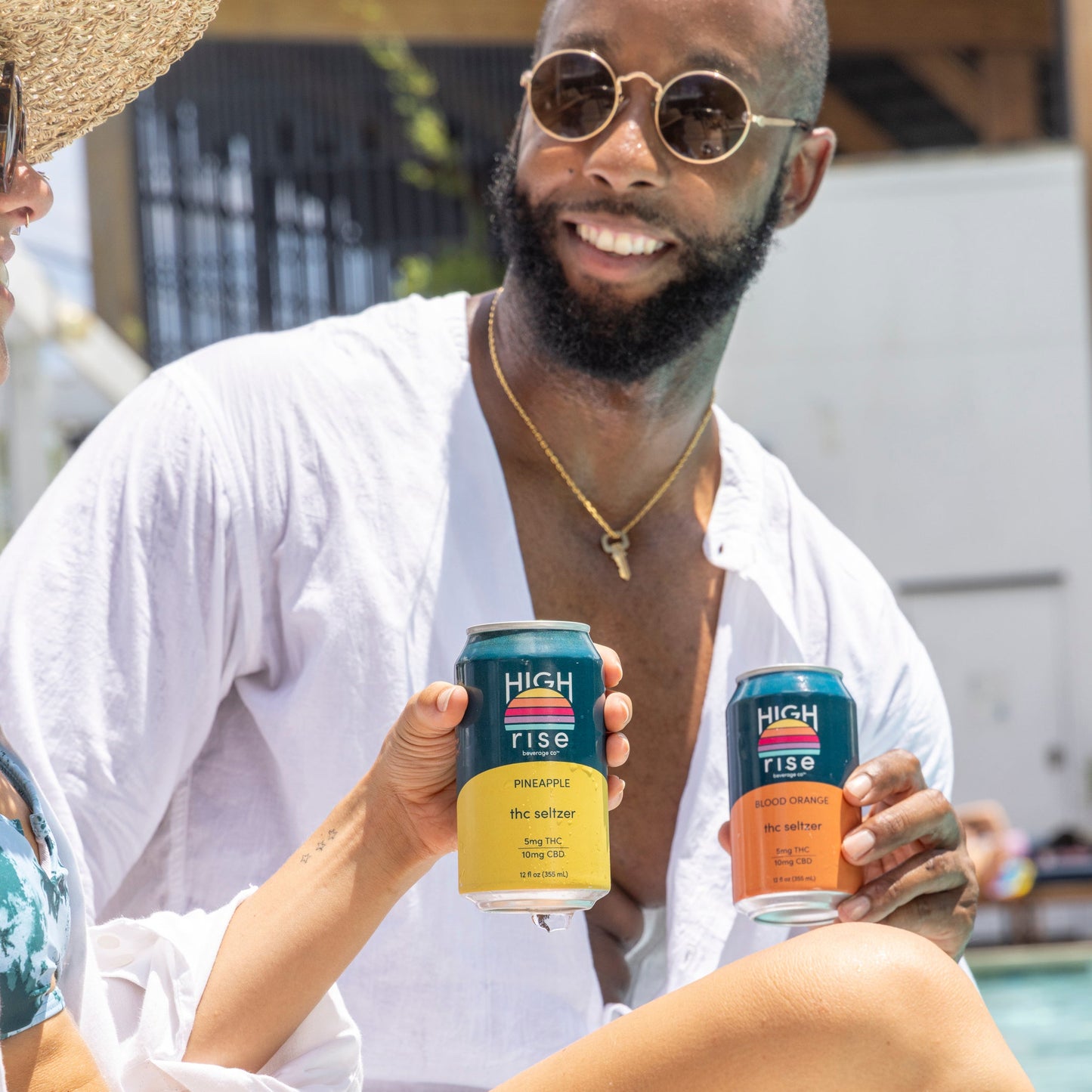Two people sitting by a pool holding Pineapple and Blood Orange Hight Rise THC cans.