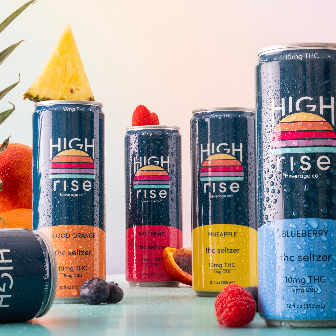 4 cans of High Rise 10mg thc seltzers standing with water condensation on the cans, making them to cold and fresh. Fruit is placed around the cans to highlight that High Rise is made with real fruit.
